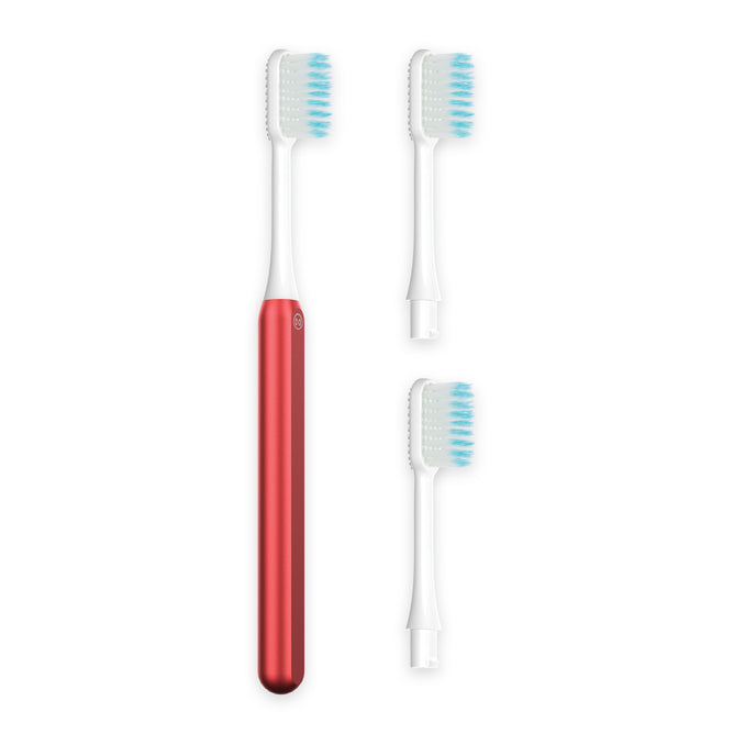 The Nada Soft Kids Toothbrush, in red and white, features an electric handle with two detachable heads—each with white bristles and blue-tipped ends—to help reduce waste, displayed on a clean white background.