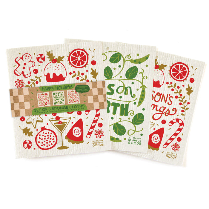 The Neighborgoods Happy Holidays Sponge Cloth Set featuring three eco-friendly Swedish sponge cloths with festive illustrations of a gingerbread man, candy cane, and citrus slices, labeled Seasons Eatings and Peas on Earth, in cardboard packaging.