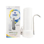 A white New Wave Enviro 10-Stage Countertop Water Filter with a curved metal spout is placed beside its colorful retail box, which highlights the benefits of this advanced filtration system.