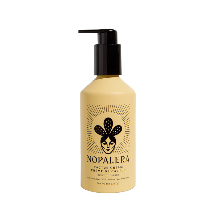 A beige bottle of NOPALERA Cactus Body Cream - Dulce De Cuerpo with a black pump. The label features a stylized face with cactus pads and sunburst rays, showcasing this prickly pear oil body nourisher for deep hydration.