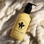 A yellow bottle of NOPALERA Cactus Shower Gel, a vegan body gel with prickly pear oil, sits on a soft white-and-beige striped towel as sunlight illuminates the scene.