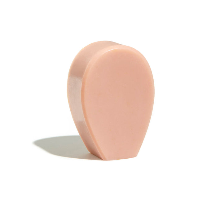 The NOPALERA Cactus Bar Soap, a pink teardrop-shaped exfoliating bar, stands upright on a white surface with a soft shadow—ideal for soothing your skin after a long day.