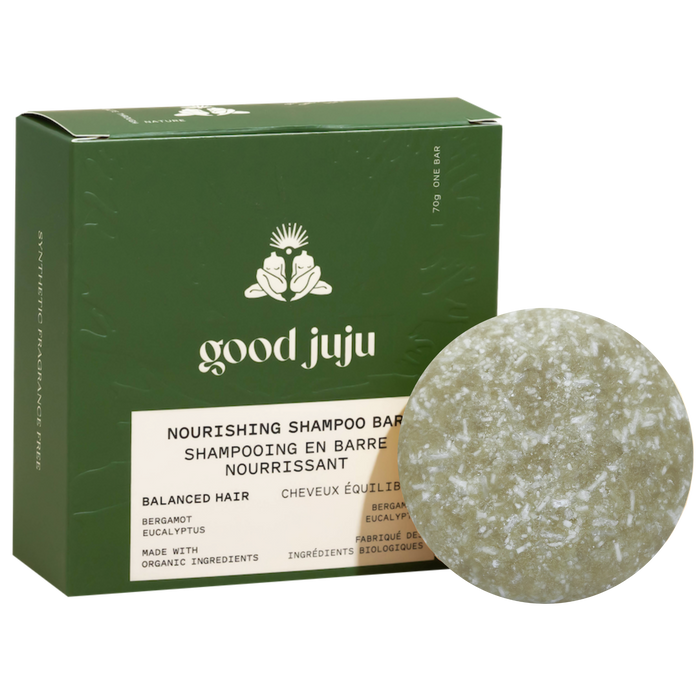 A round, green shampoo bar sits before a box labeled Good Juju Body & Home Nourishing Shampoo Bar for Balanced/Normal Hair, featuring all-natural ingredients like bergamot and eucalyptus.