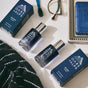 Oars + Alps ASCEND Cologne in its blue bottle and box sits on a bathroom counter beside a toothbrush, eyeglasses, blue soap, and a black-and-white striped towel—poised to deliver an enigmatic scent with every spray.