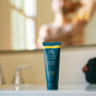 A tube of Oars + Alps Aluminum-Free Whole Body Cream Deodorant sits on a bathroom counter, with a blurred faucet and person in the background.
