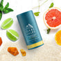 An Oars + Alps Natural Deodorant stick sits on sand among grapefruit, lime slices, green leaves, and amber stones, capturing a fresh coastal vibe.