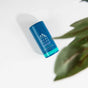 A blue Oars + Alps Natural Deodorant stick rests on a white surface beside a green plant, showcasing its odor-preventing formula and refreshing ocean splash scent.