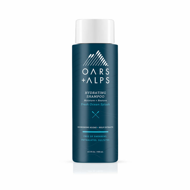 A blue bottle of Oars + Alps Hydrating Shampoo features white text and cap, highlighting Moisture + Restore, Fresh Ocean Splash scent, and notes it is sulfate-free as well as free of parabens and phthalates.