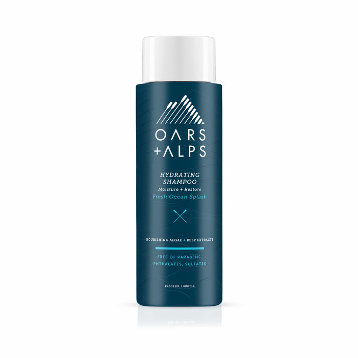 A blue bottle of Oars + Alps Hydrating Shampoo features white text and cap, highlighting Moisture + Restore, Fresh Ocean Splash scent, and notes it is sulfate-free as well as free of parabens and phthalates.