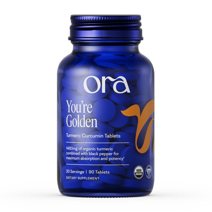 A blue Ora Organic Turmeric Curcumin Tablets bottle contains 90 tablets. The label highlights organic turmeric with black pepper, joint support, and notes it is USDA organic and vegan.