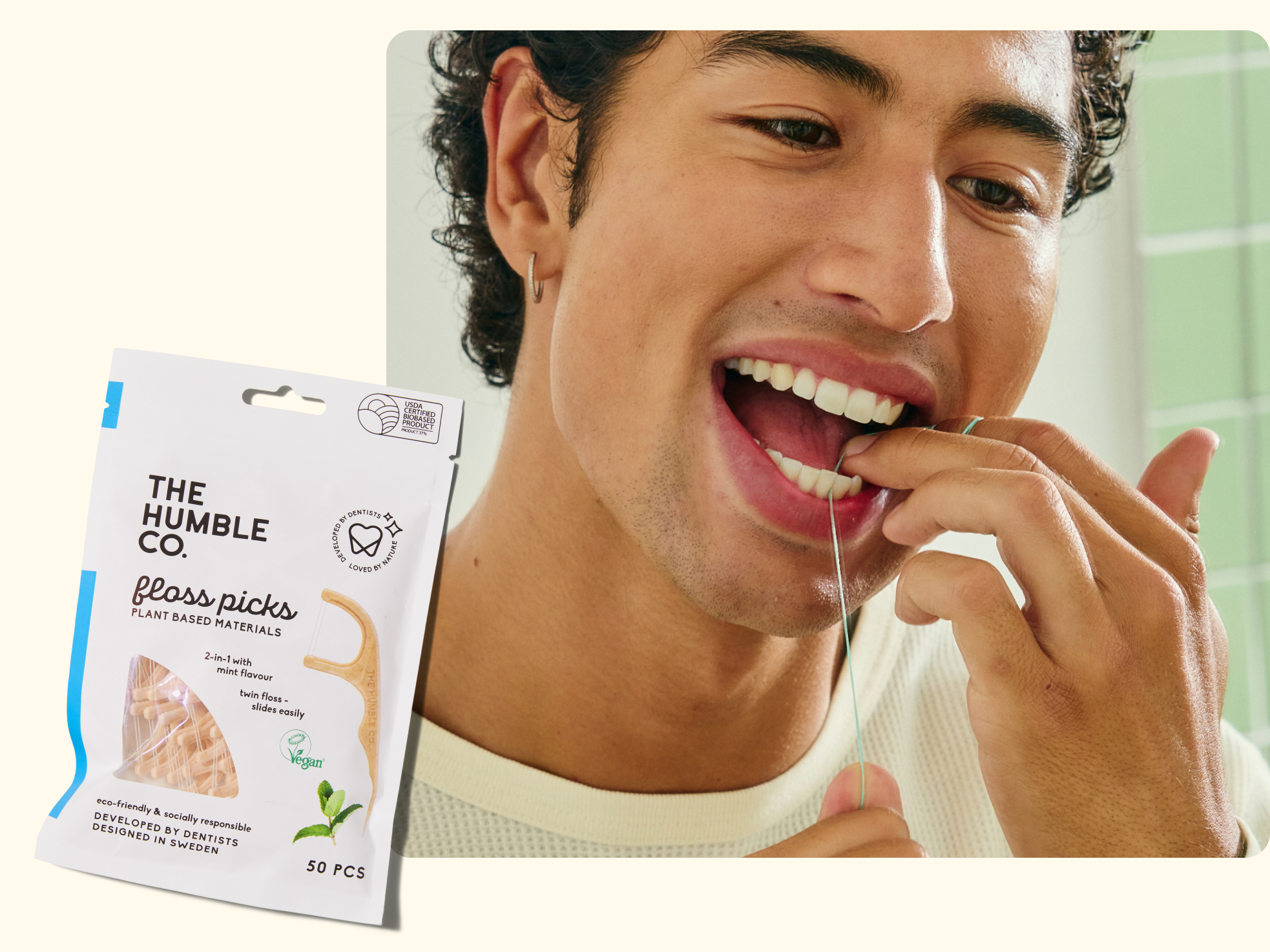 A person uses a floss pick to clean their teeth. In the foreground, a package labeled The Humble Co. Floss Picks made from plant-based materials is shown. The background is light with green tiles.