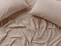 Two light brown Coyuchi Organic Crinkled Percale™ Pillowcases and a matching wrinkled bedsheet are arranged on a bed, creating a relaxed, cozy atmosphere.