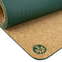 The Yoloha Yoga Original Cork Yoga Mat features a green top and cork bottom, highlighted by a circular logo with a stylized leaf and person design on the cork side. Crafted from renewable materials, this non-slip mat combines sustainability with superior grip for your practice.