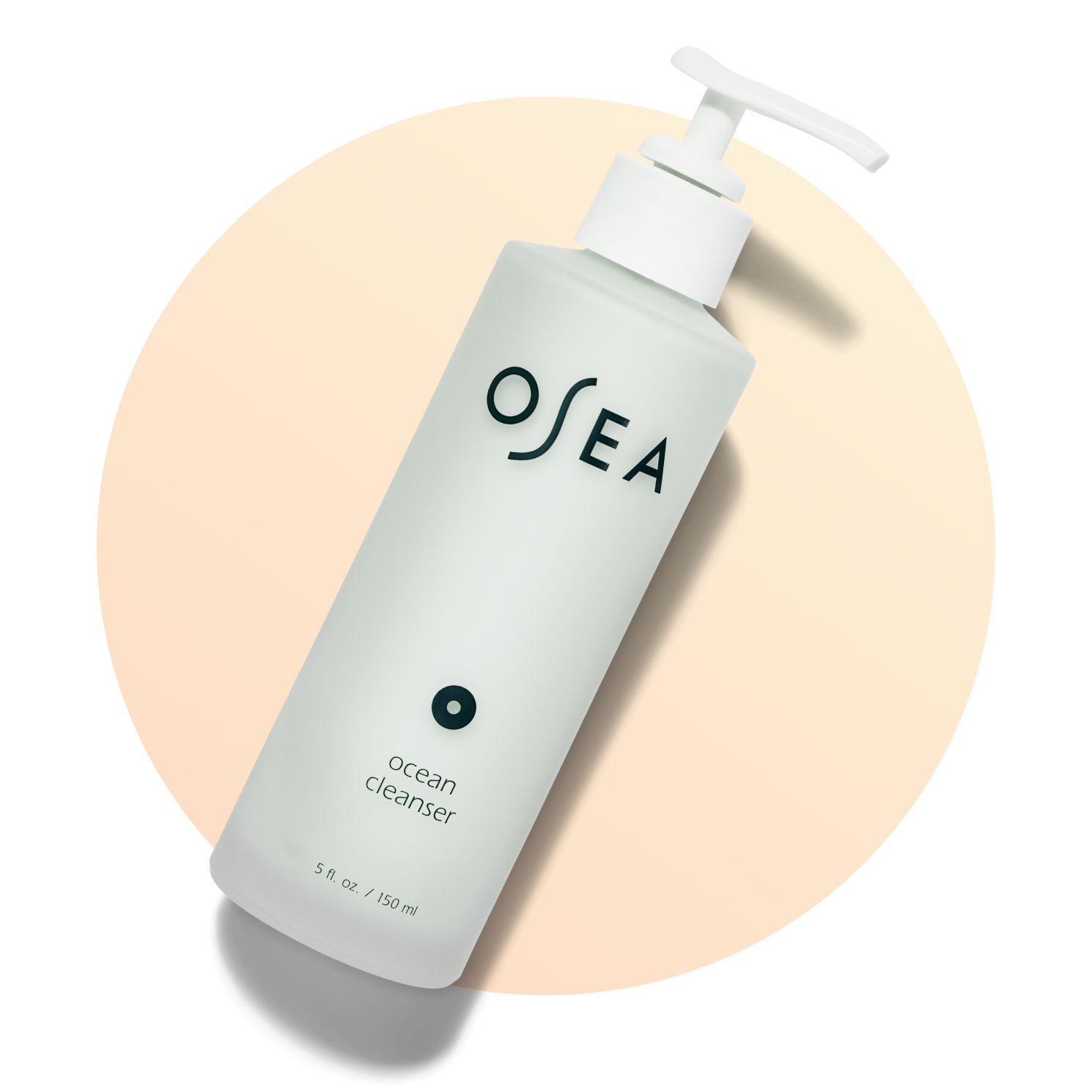 A white pump bottle labeled OSEA Ocean Cleanser lies diagonally on a light peach circular background. The bottle has minimalist black text and a clean, modern design.