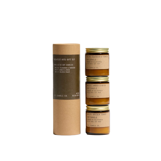 A brown cylindrical box labeled Greatest Hits Mini Candle Gift Set by P.F. Candle Co. stands beside three stacked 3.5 oz amber glass jars with gold lids, each a different scented candle, all set against a white background.
