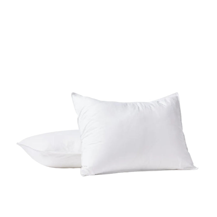 Two white Coyuchi Organic Crinkled Percale™ Shams, crafted from GOTS certified cotton, rest on a pristine white surface—one propped upright and the other lying flat behind it. The plain white background creates a clean, minimal aesthetic that accentuates the quality and softness of the organic percale beneath.