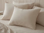Three large, cream-colored Coyuchi Organic Crinkled Percale™ Shams are arranged on a neatly made bed with matching Organic Crinkled Percale Sheets and a light wood headboard, creating a soft and cozy atmosphere.