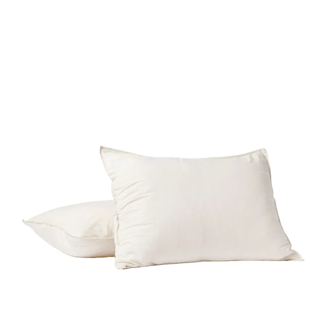 Two white pillows are displayed against a plain white background—one upright and the other lying flat just behind it—both encased in Coyuchi’s Organic Crinkled Percale™ Sham, crafted from breathable GOTS Certified organic cotton.