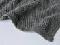 A close-up of a textured gray Coyuchi Air Weight® Organic Towel with a wavy edge, resting on a light surface.