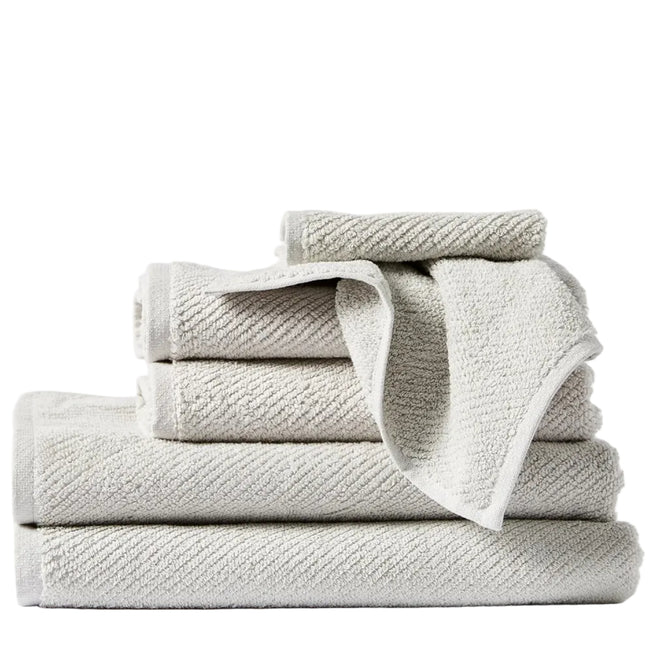 A neatly stacked set of four Coyuchi Air Weight® Organic Towels in light gray, made from premium bathroom towel material, with one towel draped over the stack and a small towel rolled on top, all set against a plain white background.