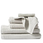 A neatly stacked set of four Coyuchi Air Weight® Organic Towels in light gray, made from premium bathroom towel material, with one towel draped over the stack and a small towel rolled on top, all set against a plain white background.