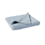 A neatly folded Air Weight® Organic Towel by Coyuchi in light blue rests on a white background. One corner of the organic cotton towel is flipped over, highlighting its textured surface, plush thickness, and absorbent quality.