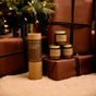 Brown gift-wrapped presents and the P.F. Candle Co. Greatest Hits Mini Candle Gift Set, 3.5 oz—featuring amber jars with minimalist labels—are arranged under a Christmas tree, creating a cozy, festive atmosphere with warm lights.