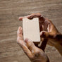 Two hands lather the rectangular white Everything Bar by Phil's, enriched with upcycled plant squalane, against a beige textured background.