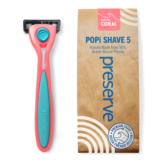 A coral and teal Preserve Recycled Ocean Plastic (POPi) Shave 5 Razor System sits beside brown packaging labeled “POPi SHAVE 5”, highlighting its handle made from 90% ocean-bound plastic. The package displays eco-friendly and premium shave icons, emphasizing the sustainable design of this razor by Preserve.