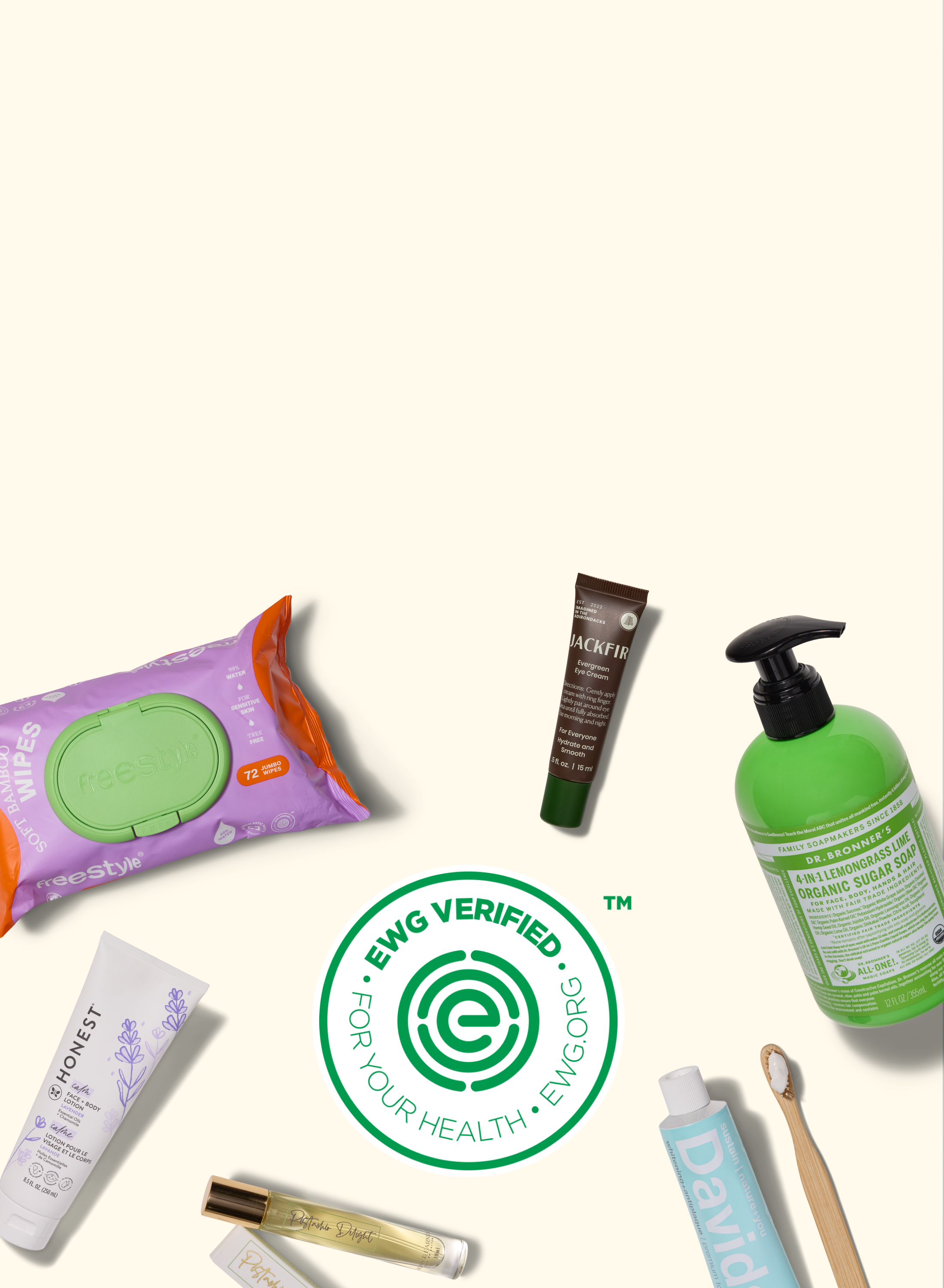 A flat lay of personal care products, including wipes, lotion, toothpaste, soap, a toothbrush, and a tube of balm, arranged around an “EWG VERIFIED” green circular logo on a beige background.