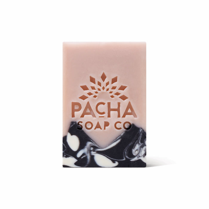 A rectangular Pacha Soap Co. Bar Soap features a pink top, black and white marbled bottom, and an engraved sunburst logo, blending natural exfoliants for a gentle cleanse.