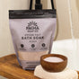 A bag of Pacha Soap Co. Sleep Epsom Salt Bath Soak sits beside a wooden bowl of soak powder and a folded towel, arranged at the edge of a bathtub.