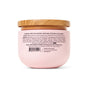 A pink jar of Pacha Soap Co. Body Scrub with a wooden lid features a back label listing directions, ingredients, and cautions for its gentle pumice exfoliant; barcode and company details are at the bottom.
