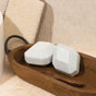 Two light blue, geometric Breathe Epsom Salt Bath Bombs by Pacha Soap Co. rest on a wooden tray with a small spoon. A beige cloth and white container complete the calm, minimalist aromatherapy-inspired setting.