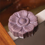 The French Lavender Froth Bomb by Pacha Soap Co., shaped like a purple flower, sits on a bathtub edge—ready to infuse your soak with nourishing lavender essential oil.