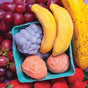 A close-up of fresh grapes, strawberries, and a banana surrounds Pacha Soap Co.'s Fruit Basket Bath Bomb Set—fun, fruit-shaped kids bath bombs designed to look like bananas, grapes, and peaches.