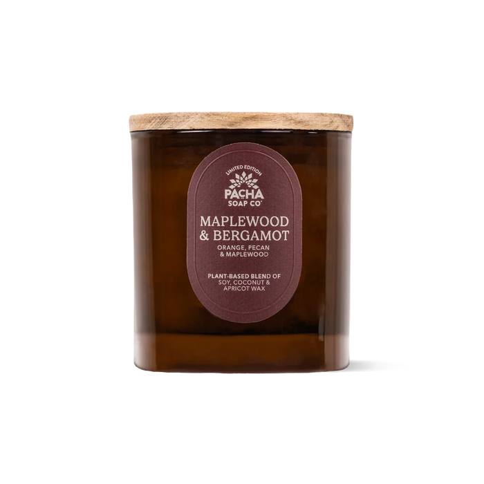 Amber glass candle jar with a wooden lid and a label that reads MAPLEWOOD & BERGAMOT, highlighting house-designed fragrances and plant-based wax, from the Fall Signature Candle collection by Pacha Soap Co., displayed on a plain white background.