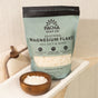 A bag of Pacha Soap Co. Salt Soak labeled “Sea Salt & Moss” sits on a bathtub edge beside a wooden bowl of salt soak, a folded towel, and a wooden scoop—perfect for creating a relaxing bath experience.