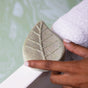 A hand holds Pacha Soap Co.'s Vanilla & Sage Bath Bomb beside a white towel near a bathtub filled with water, setting a relaxing scene.