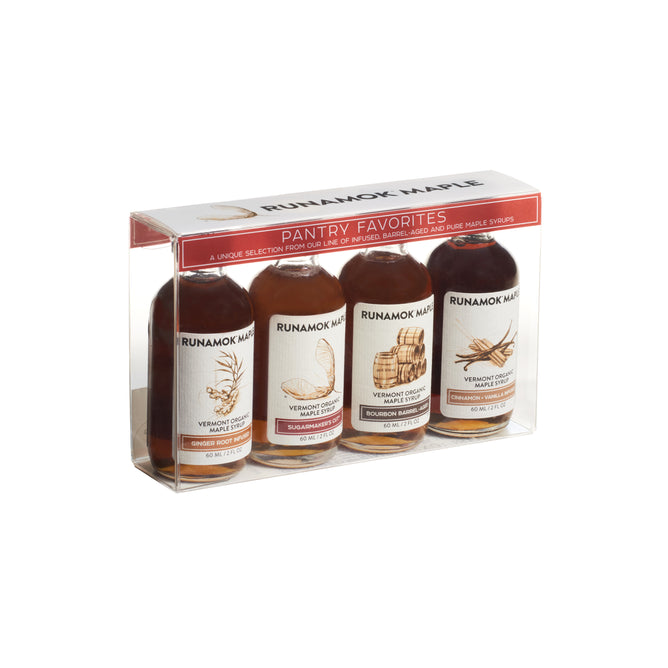 A clear gift box of four Runamok Pantry Favorites Pairing Collection syrups, each bottle uniquely labeled and illustrated. This maple syrup sampler showcases amber syrups from the Runamok brand, arranged neatly side by side.