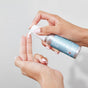 A person with manicured nails dispenses a small amount of Plaine Products Styling Gel onto their fingers against a plain background.
