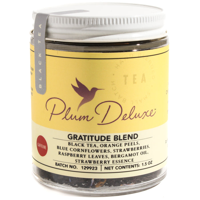 A jar of Plum Deluxe Gratitude Strawberry Earl Grey Tea with a yellow label, featuring black tea blended with orange peels, blue cornflowers, strawberries, raspberry leaves, and bergamot oil.