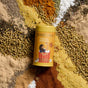 A yellow Diaspora Spice Co. Popcorn Seasoning can sits among an array of vibrant single-origin spices—coriander seeds, turmeric, chili powder, cumin seeds, and salt—all sourced from regenerative farms and spread out on a flat surface.