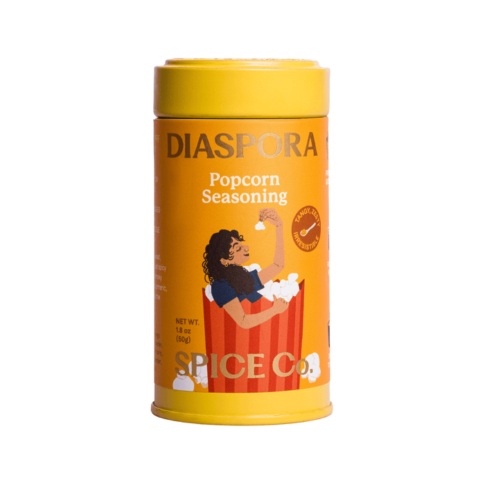 A yellow Diaspora Spice Co. Popcorn Seasoning tin featuring an illustration of a woman enjoying popcorn while sitting in a striped popcorn bucket—crafted with single-origin spices from regenerative farms for the ultimate nutritional yeast popcorn seasoning experience.