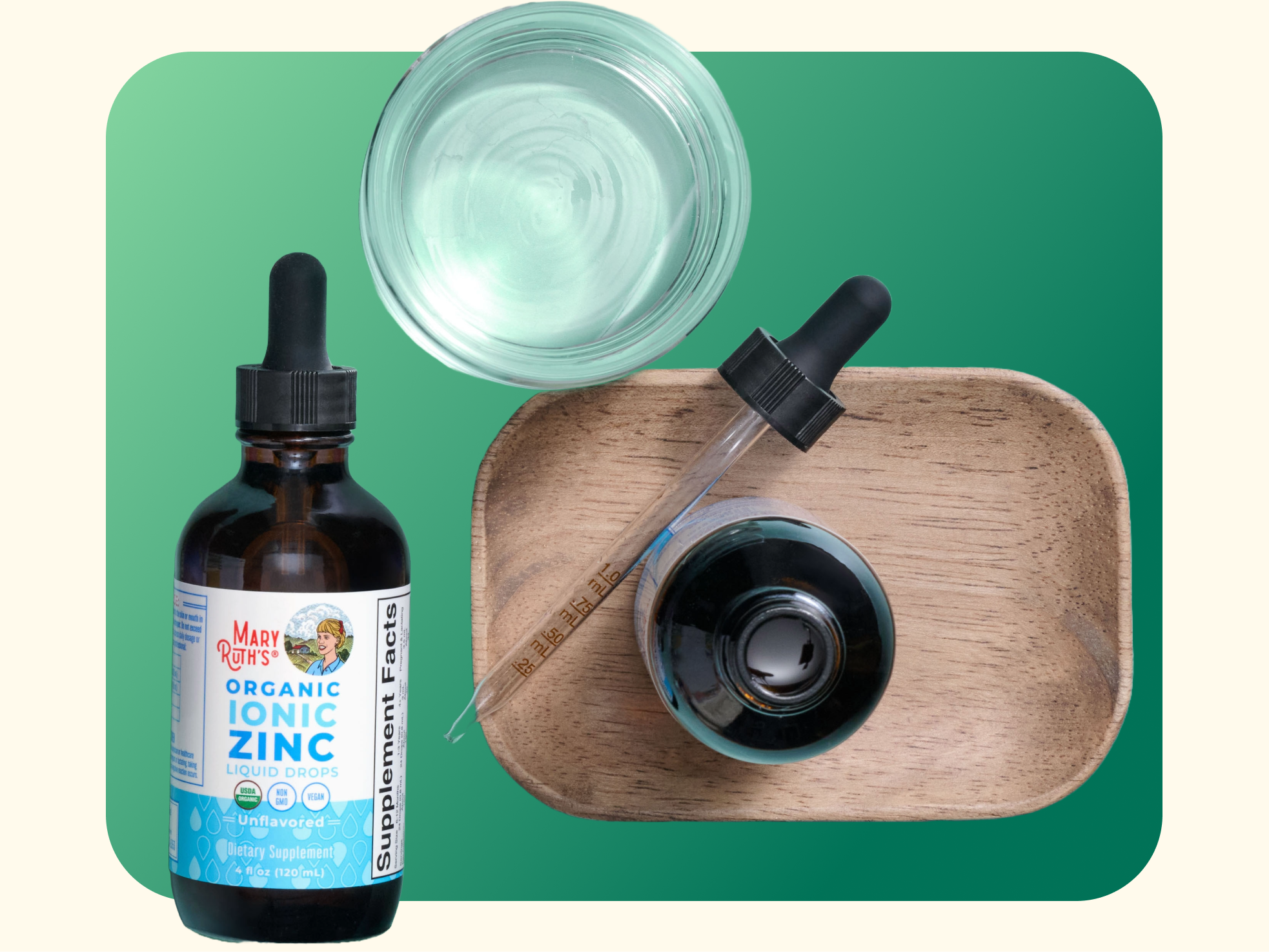 A bottle of MaryRuth’s Organic Ionic Zinc liquid drops with a dropper, a small wooden tray, and a glass of clear liquid on a green background.