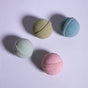 Four round Froth Bomb bath bombs from Pacha Soap Co.'s Pacha Peaces set in pastel green, blue, light blue, and pink rest on a textured white surface, casting soft shadows.