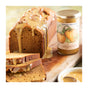 A loaf of pumpkin bread with golden glaze sits beside a jar of Savannah Bee Company Pumpkin Spice Whipped Honey, a creamy spreadable delight, all arranged on a wooden cutting board.