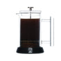 The Pure Over French Press Coffee Maker, made of borosilicate glass, sits on a black base against a white background with the plunger pressed down, brewing rich coffee.