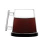 The Pure Over Signature Mug (14 oz), made of borosilicate glass with a modern cylindrical handle, filled with dark coffee, rests on a ceramic coaster against a white background.