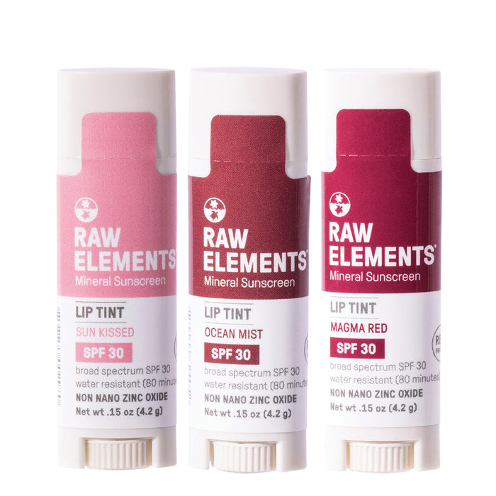 Three Raw Elements Tinted Lip SPF 30 .15 oz Sunrise Pack products stand side by side with shades: Sun Kissed, Ocean Mist, and Magma Red. They offer a sun-kissed glow with organic ingredients and broad-spectrum UVA-UVB protection. The sleek white packaging features bold text and a sun icon.